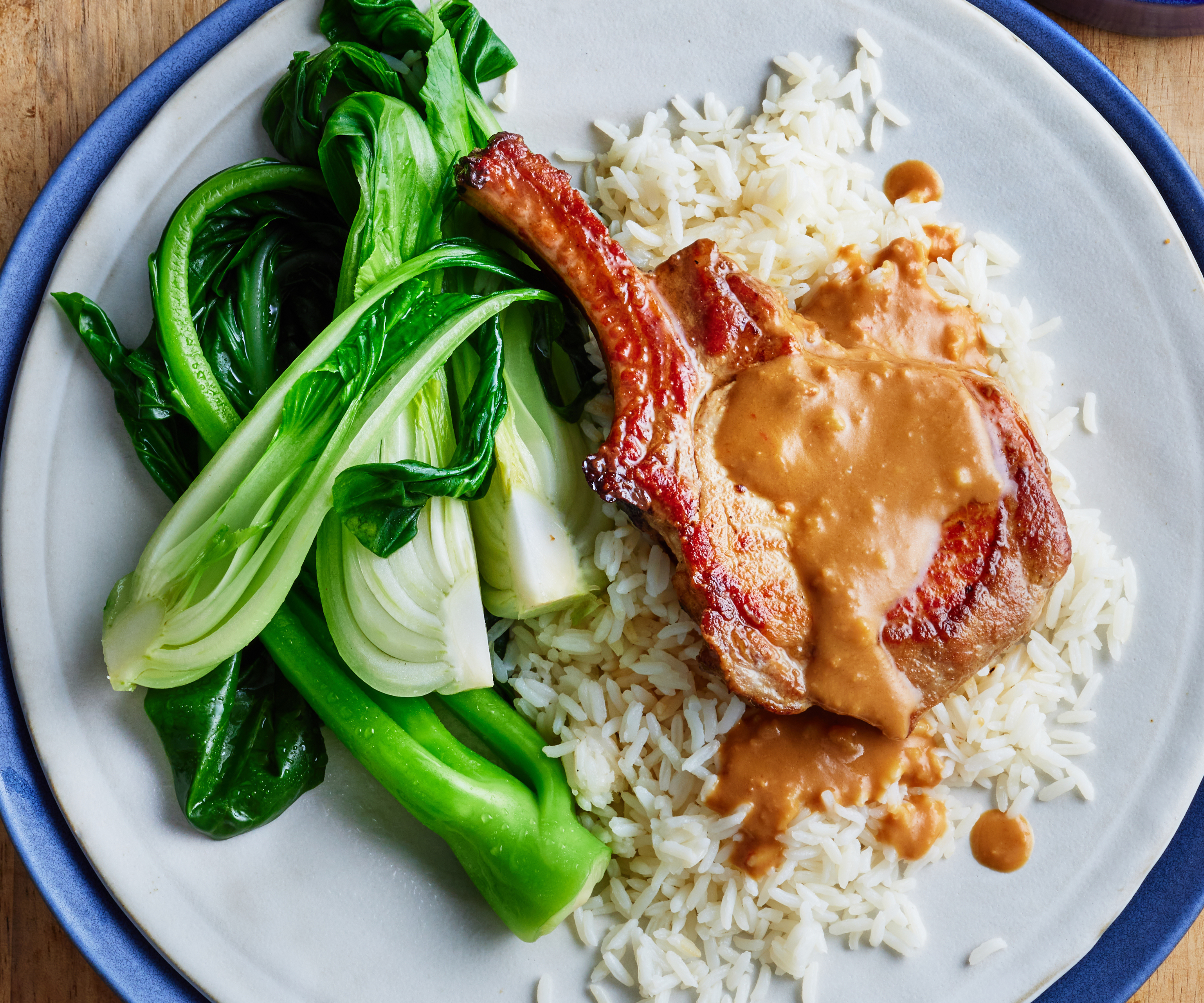 Plate with rice, bok choy and a large pork cutlet with sticky peanut sauce poured on top.
