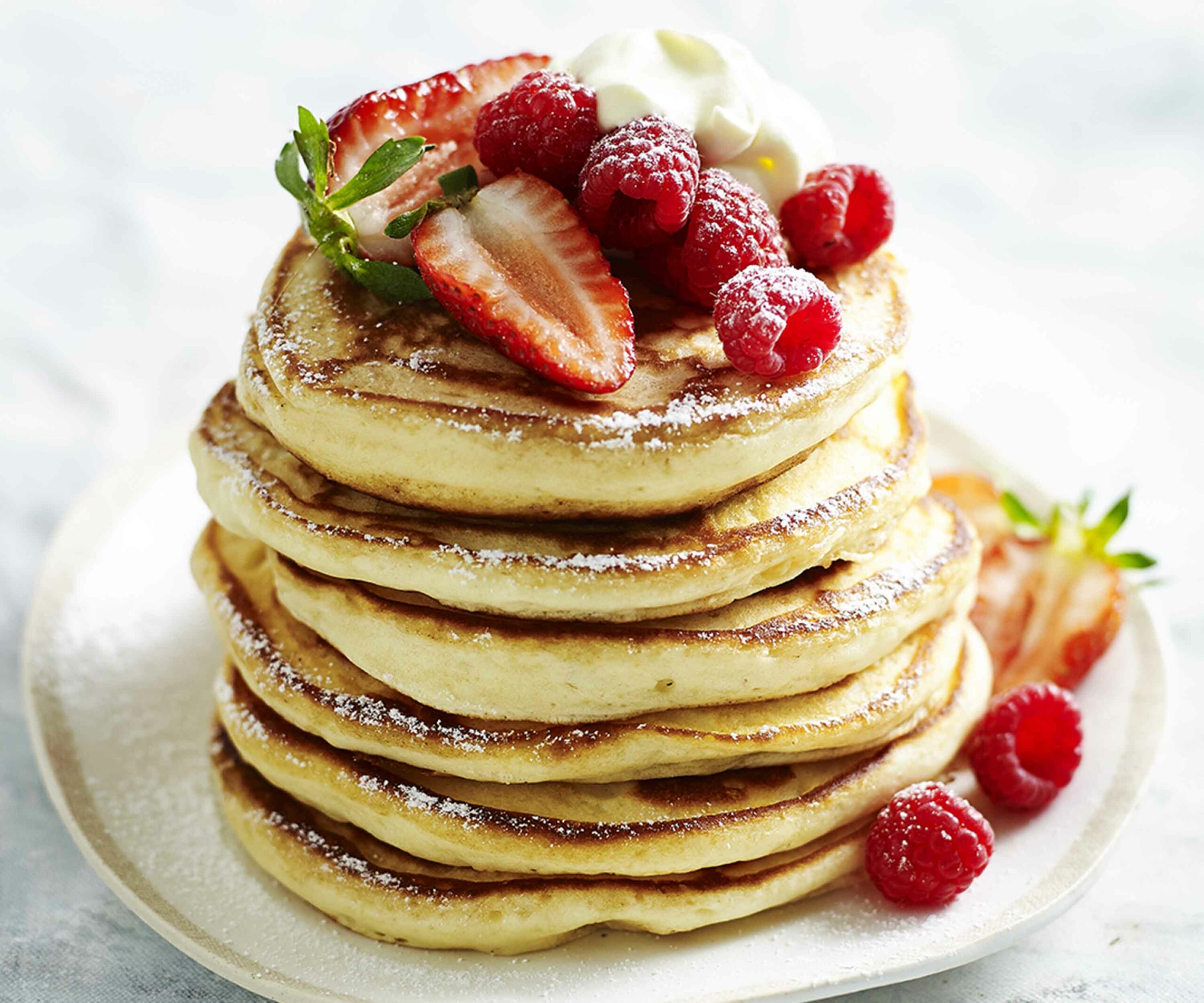 a stack of pancakes on a plate, topped with berries