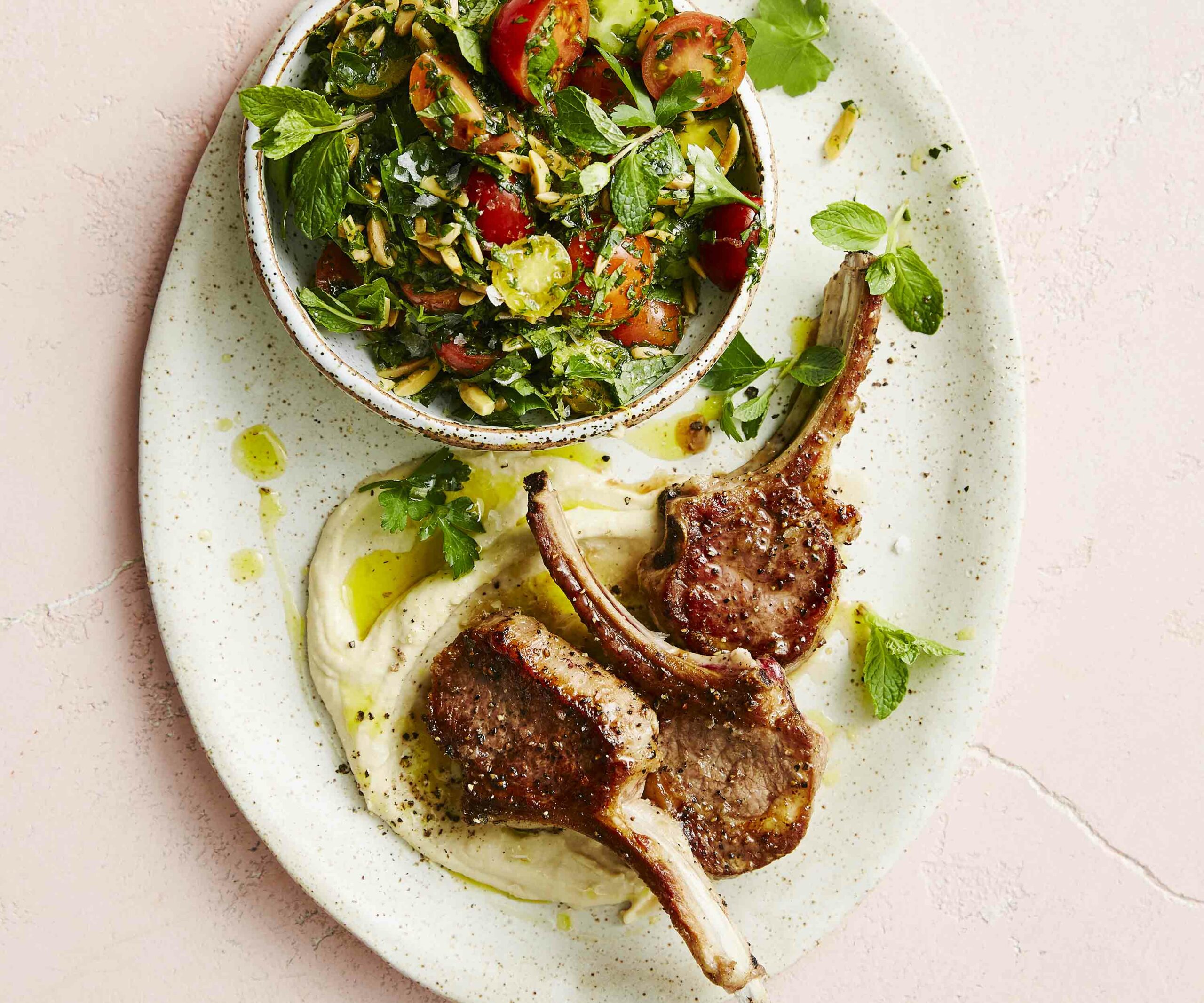 Three lamb cutlets on a plate with hummus and tabbouleh in a bowl
