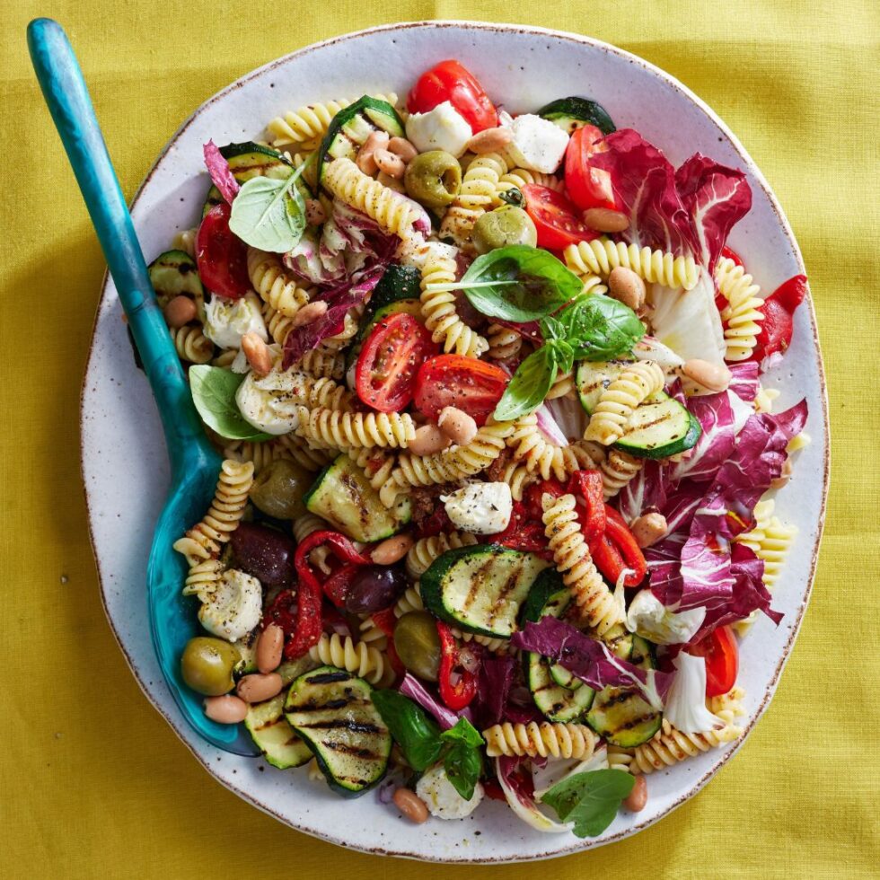 pasta salad on an oval bowl with blue spoon on a yellow background