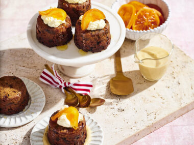 Mini Christmas puddings on a cake stand and plate with a jug of brandy sauce