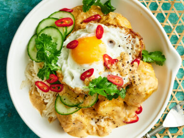 Potato rendang in a bowl, served with rice and a crispy fried egg. Garnished with cucumber and chilli.