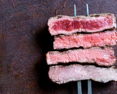 Four pieces of red meat, such as a cut of a steak, cooked and skewered on a fork.