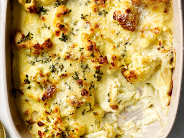 Cauliflower cheese with leek and fennel in a large dish with a scoop taken out, ready to serve.